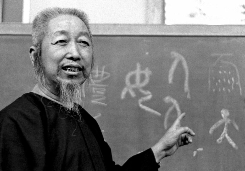 Photo historique du maître Zheng Manqing enseignant le Tai Chi Chuan style Yang devant un tableau d’écriture chinoise traditionnelle.